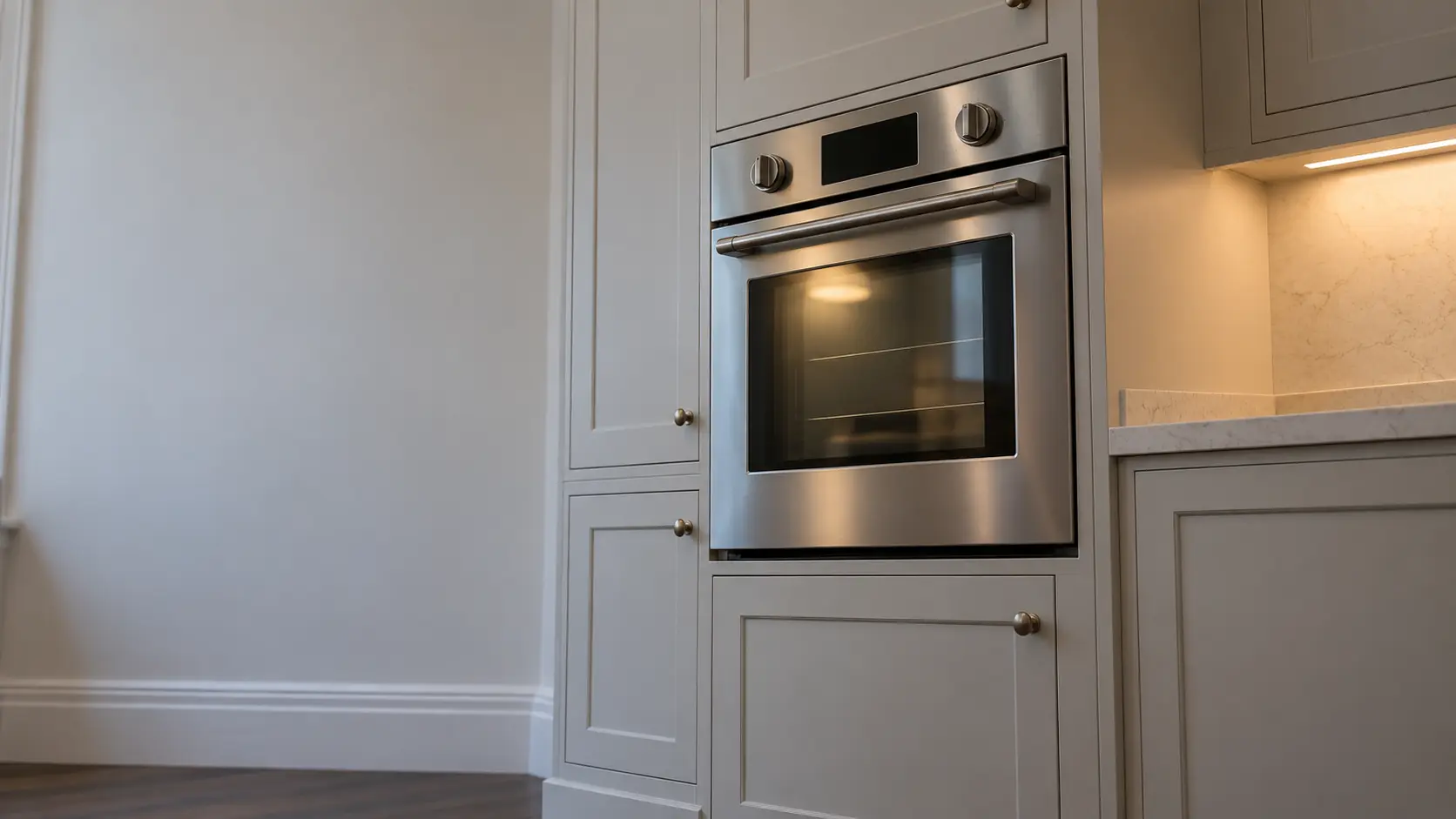 A kitchen wall with the oven in a Victorian flat kitchen with a compact wall oven, seen from a low angle, the oven door glass catching the light.