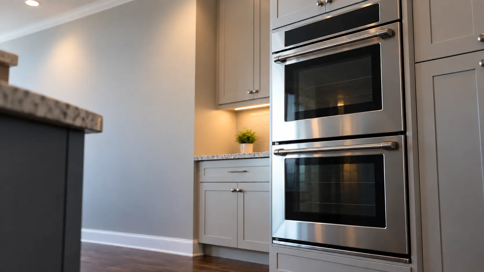 A kitchen wall with the oven in a suburban split-level kitchen with a double wall oven, seen from a low angle, the oven door glass catching the light.