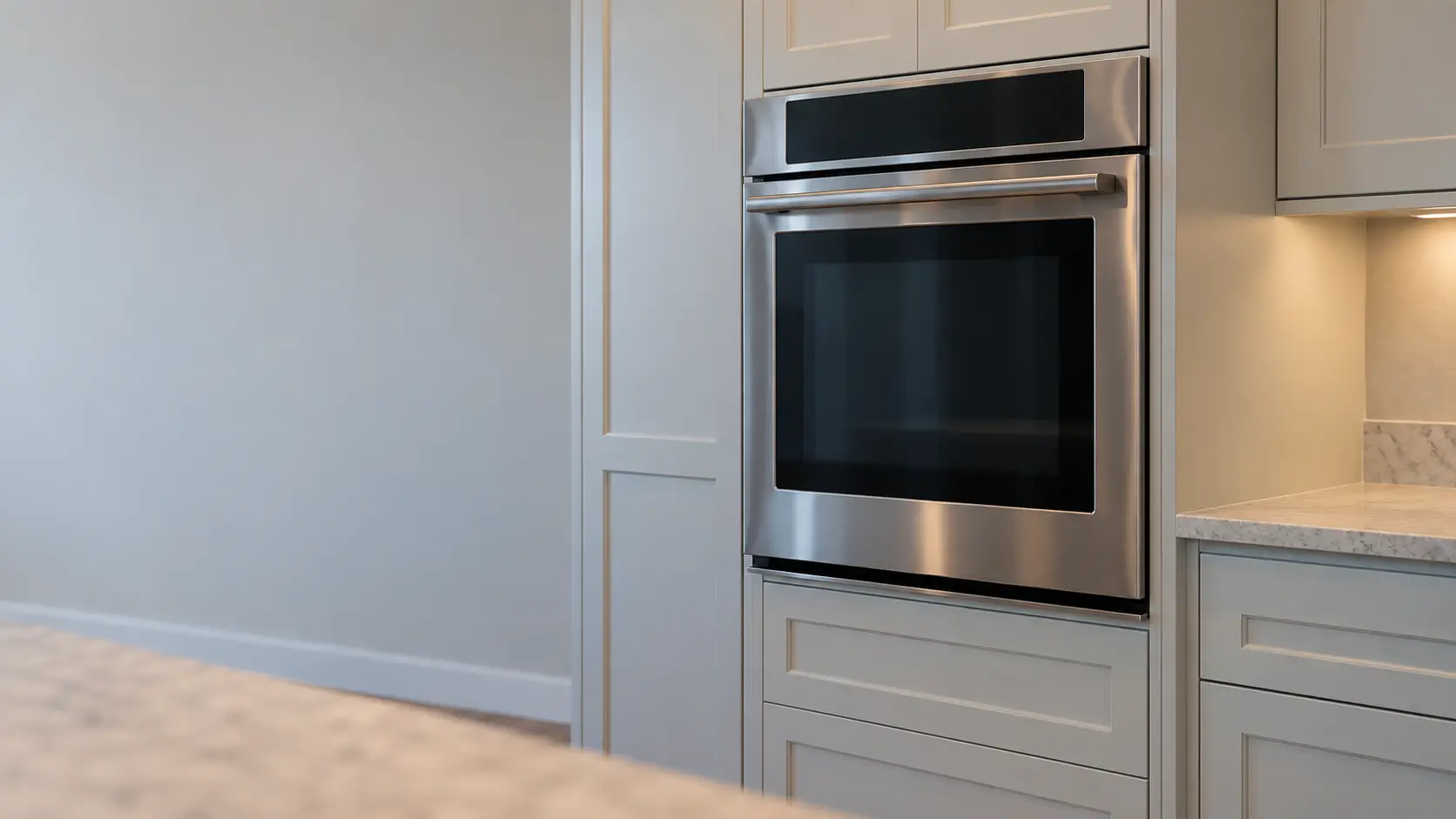 A kitchen wall with the oven in a raised coastal house kitchen with a single wall oven, seen from a low angle, the oven door glass catching the light.