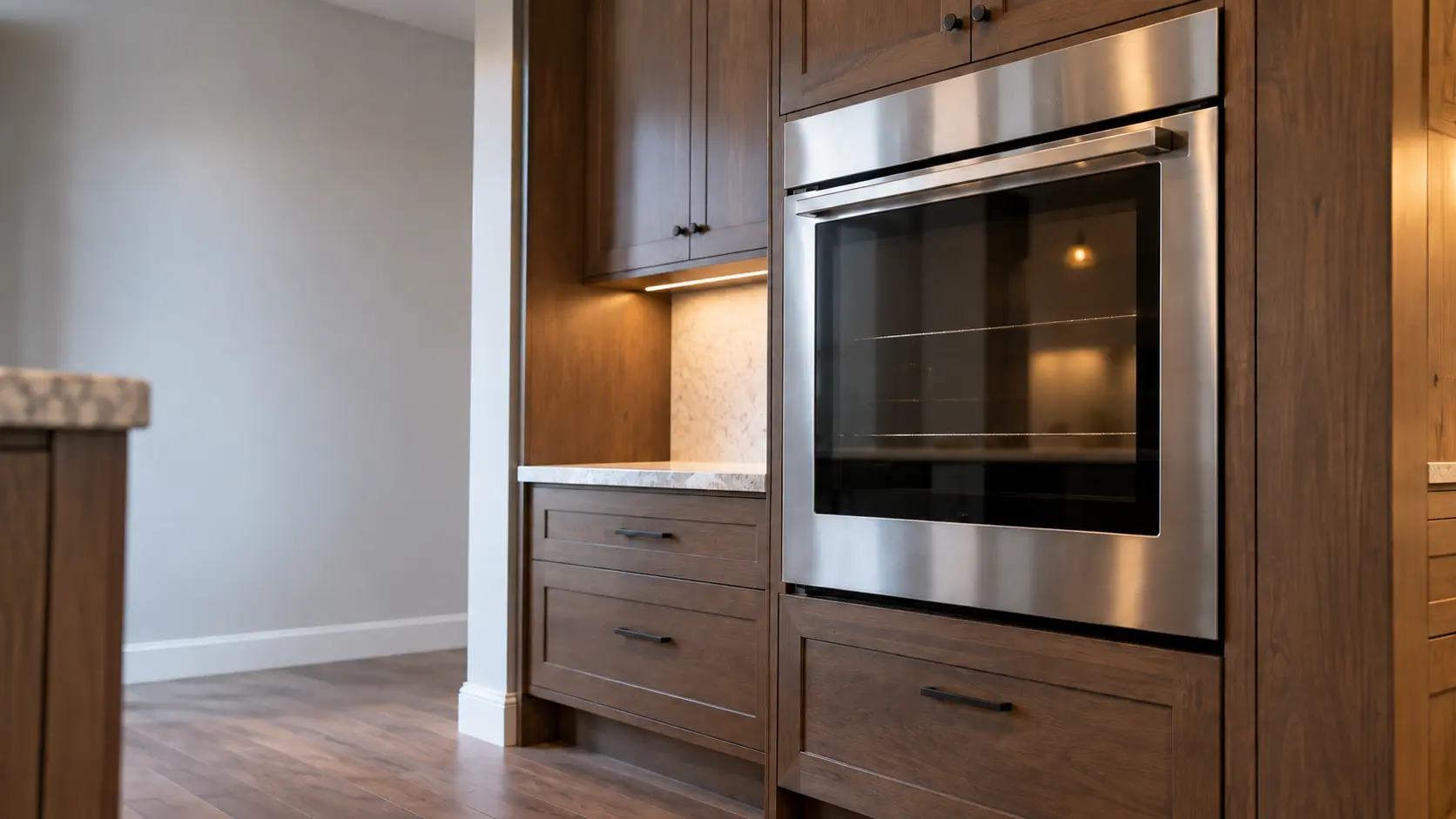 A kitchen wall with the oven in a wooded-lot house kitchen with a wall oven in stained cabinets, seen from a low angle, the oven door glass catching the light.