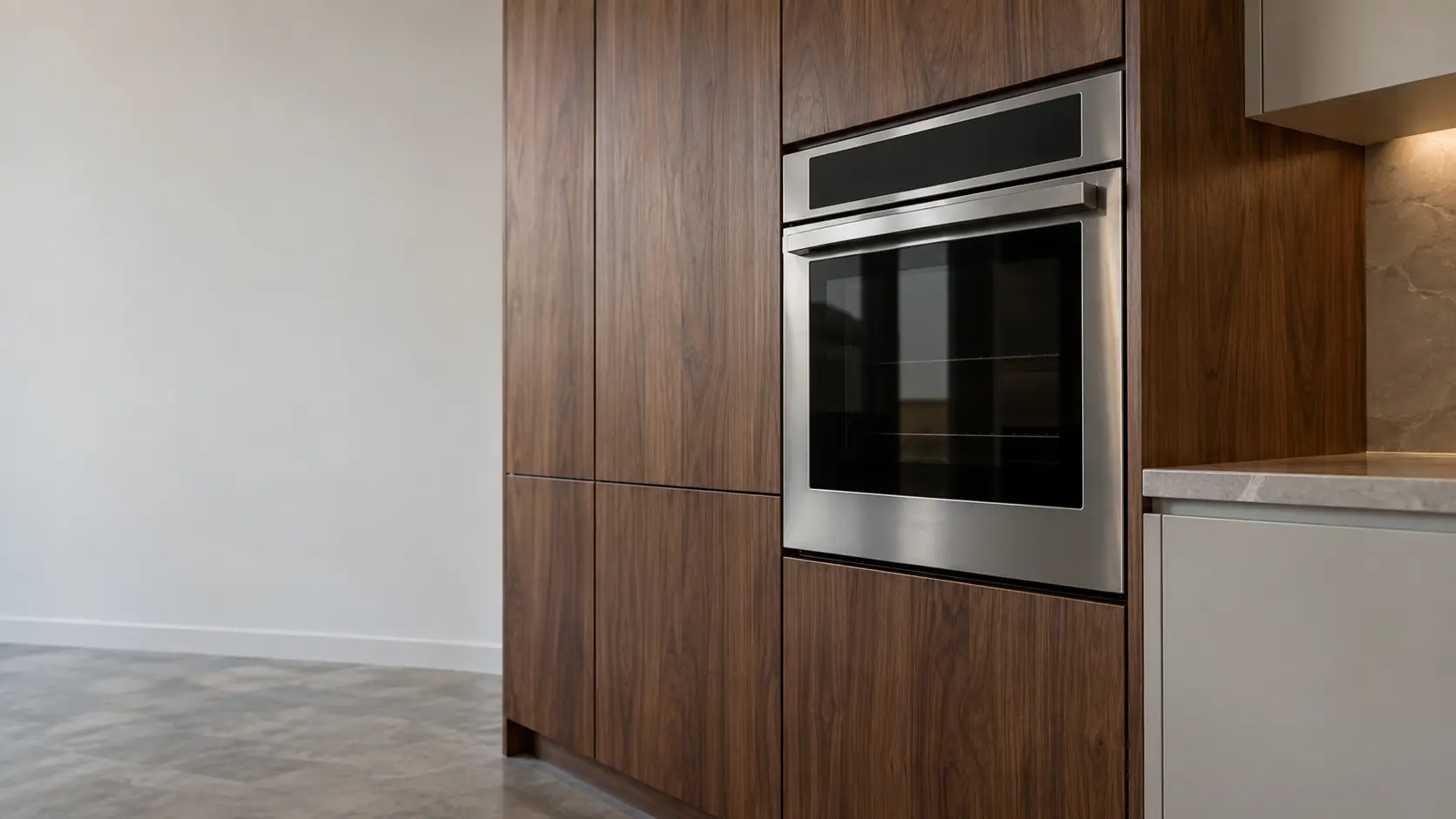 A kitchen wall with the oven in a mid-century house kitchen with a wall oven in walnut cabinets, seen from a low angle, the oven door glass catching the light.