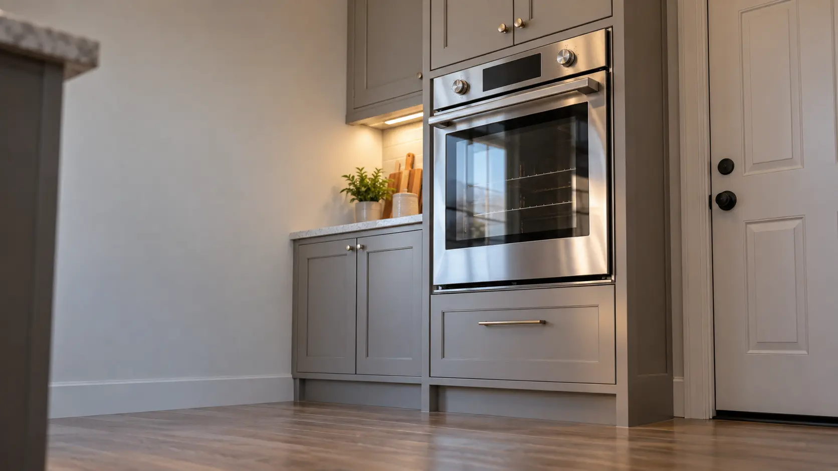A kitchen wall with the oven in a semi-attached house kitchen with a wall oven beside the back door, seen from a low angle, the oven door glass catching the light.