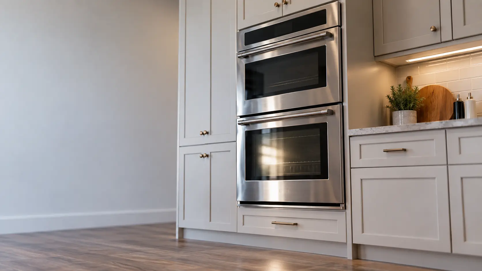 A kitchen wall with the oven in a detached house kitchen with a double wall oven, seen from a low angle, the oven door glass catching the light.