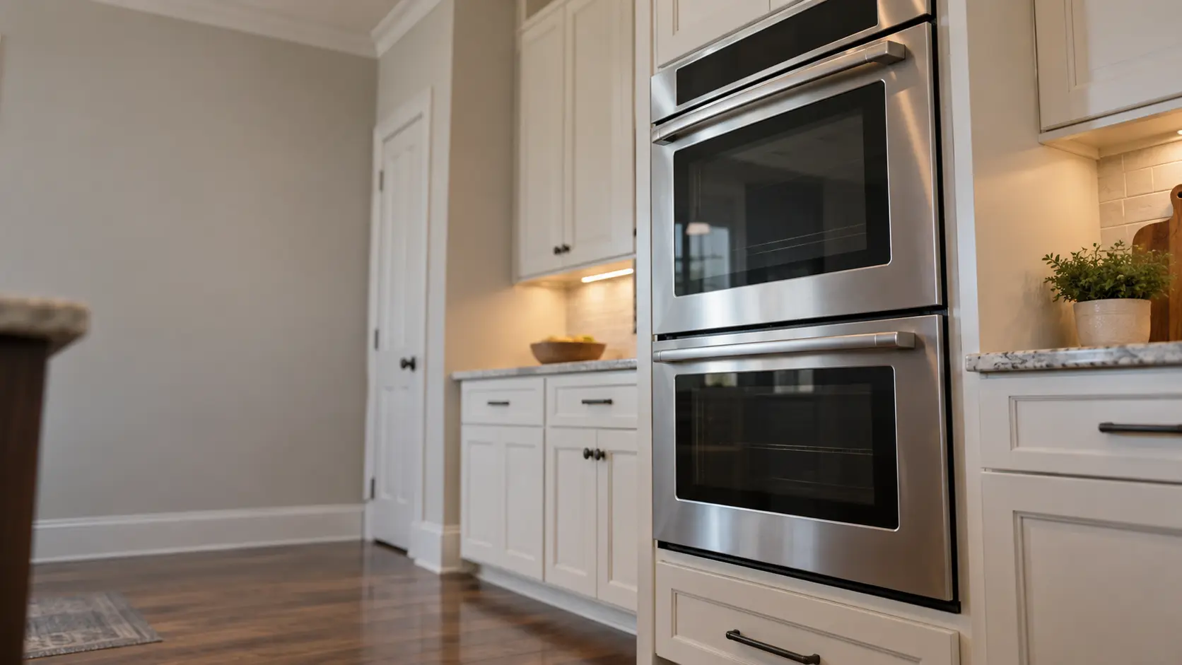 A kitchen wall with the oven in a suburban Tudor house kitchen with a double wall oven, seen from a low angle, the oven door glass catching the light.