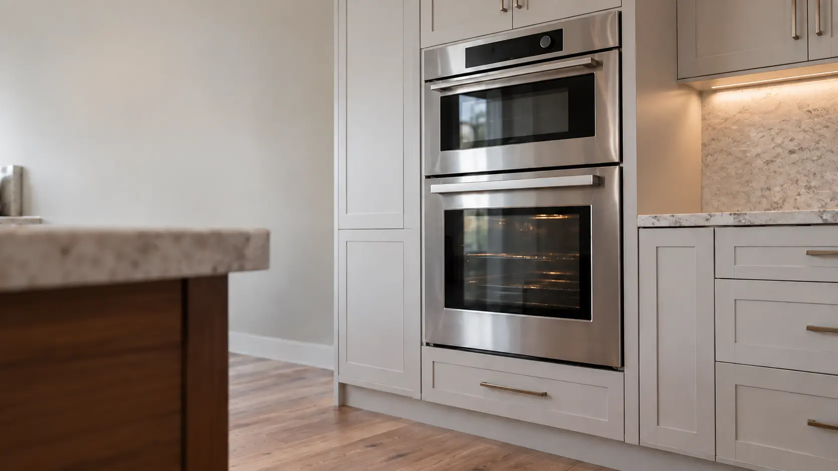 A kitchen wall with the oven in a hillside ranch house kitchen with a wall oven and steam oven, seen from a low angle, the oven door glass catching the light.