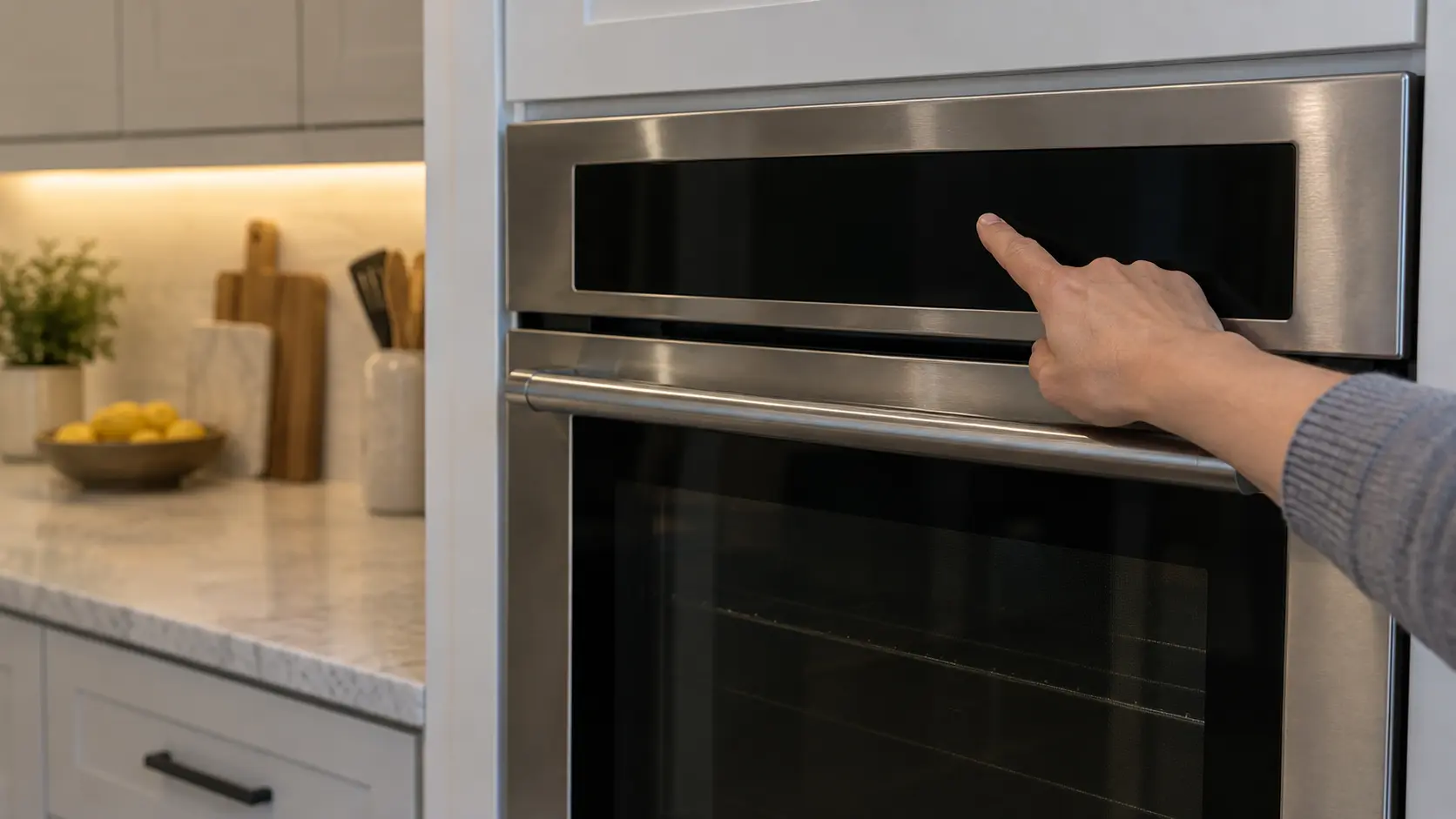 A finger pressing the dark touch control strip above a stainless wall oven in a US home kitchen, the display unlit.