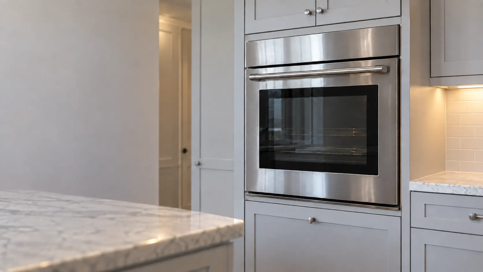 A stainless single wall oven is set into a painted cabinet at chest height in a bright US home kitchen.