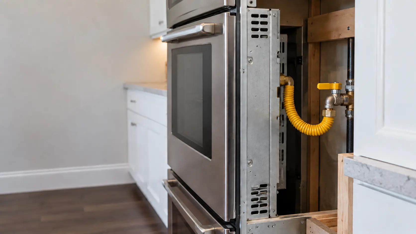 Close on a yellow-coated gas connector and shutoff valve behind a gas wall oven.