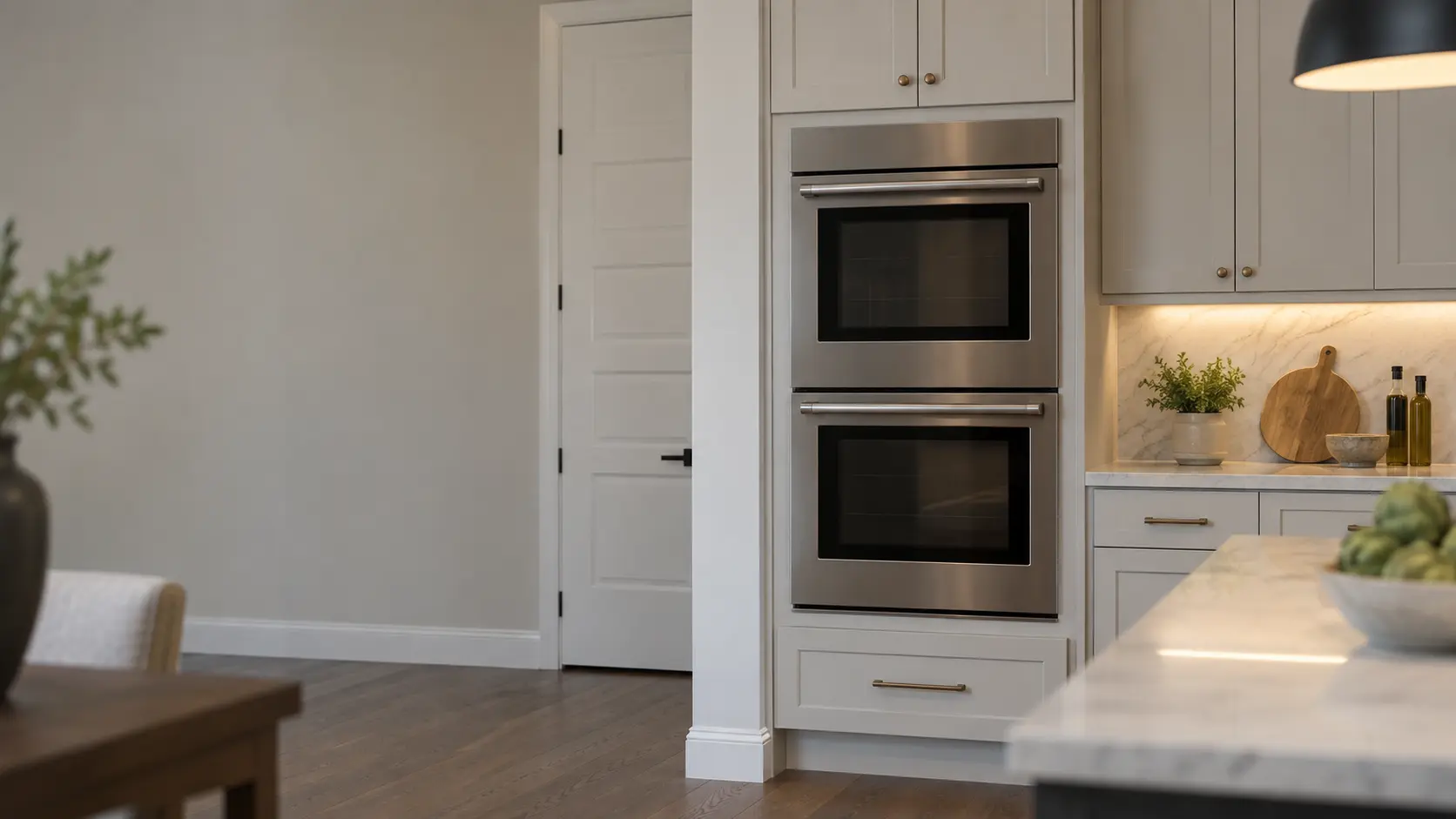 A built-in wall oven in a large Texas suburban kitchen with a double wall oven in tall painted cabinets and a walk-in pantry door, seen square on from across the room.
