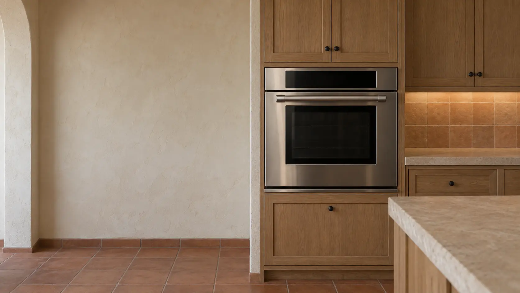 A built-in wall oven in a Spanish-style Los Angeles kitchen with a wall oven set into plaster walls and terracotta tile, seen square on from across the room.