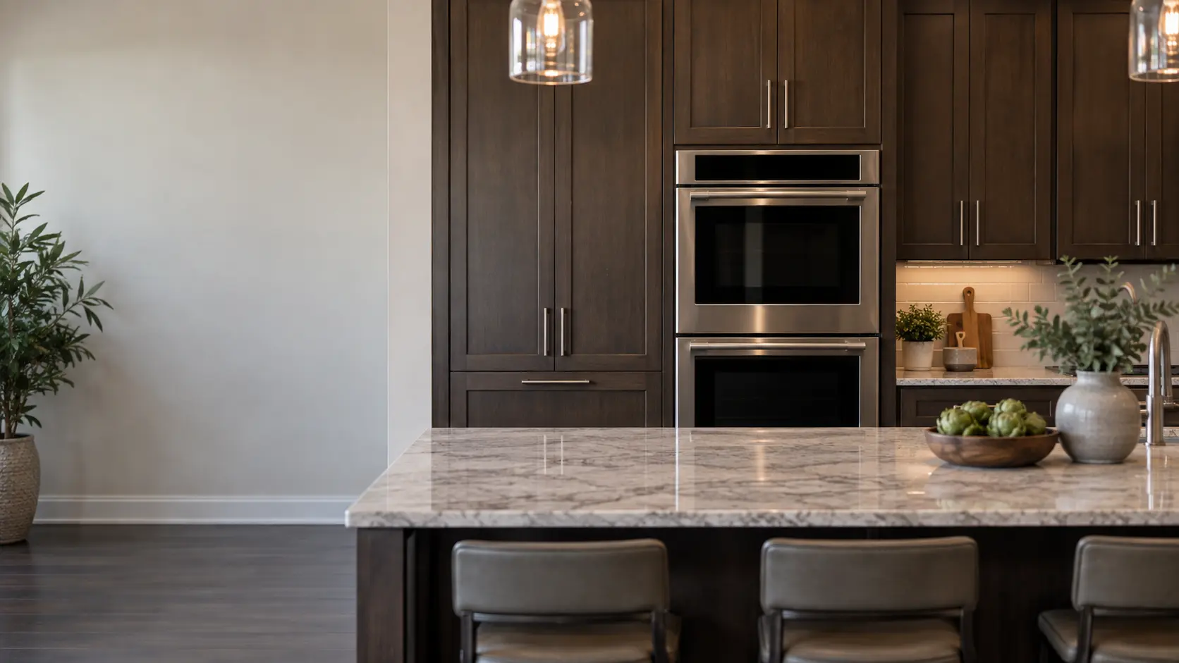 A built-in wall oven in a newer Central Florida kitchen with a double wall oven in a run of tall espresso cabinets and a large island, seen square on from across the room.